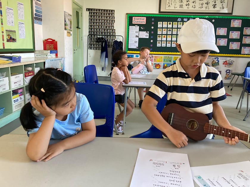 Building Student Confidence: Strategies That Work 1 Lower school student playing guitar in a colorful classroom while a classmate watches attentively, illustrating confidence through creative performance