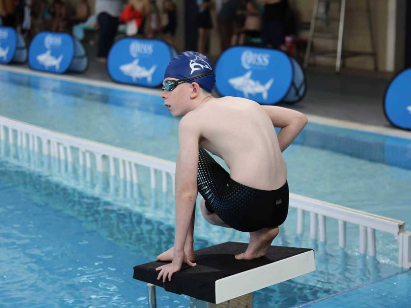 Building Student Confidence: Strategies That Work 3 Young student in school swim cap and goggles standing on a diving board at an indoor pool, preparing to dive at a competitive swim event