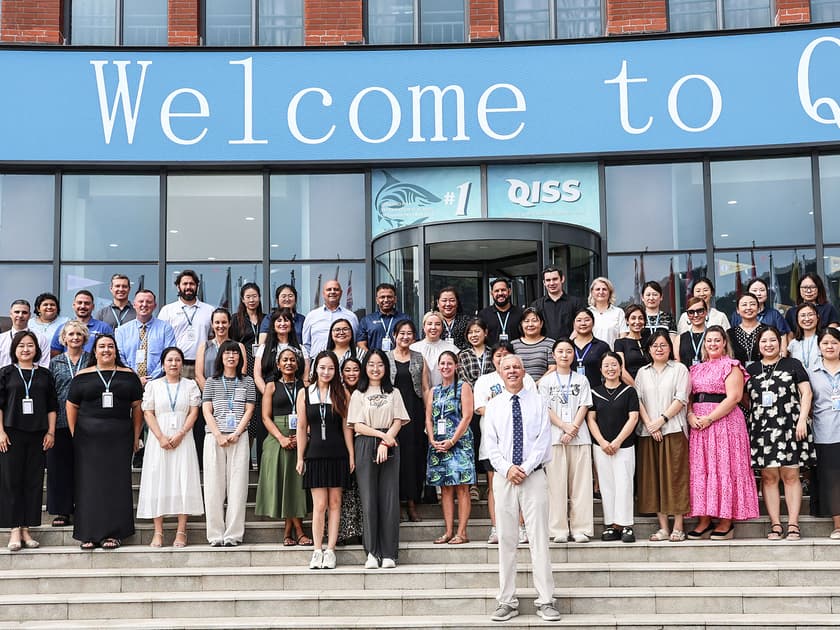 Chinese Language Programs in International Schools 3 QISS faculty and staff gathered at the school entrance under a Welcome to QISS banner, representing the school's community in Qingdao.