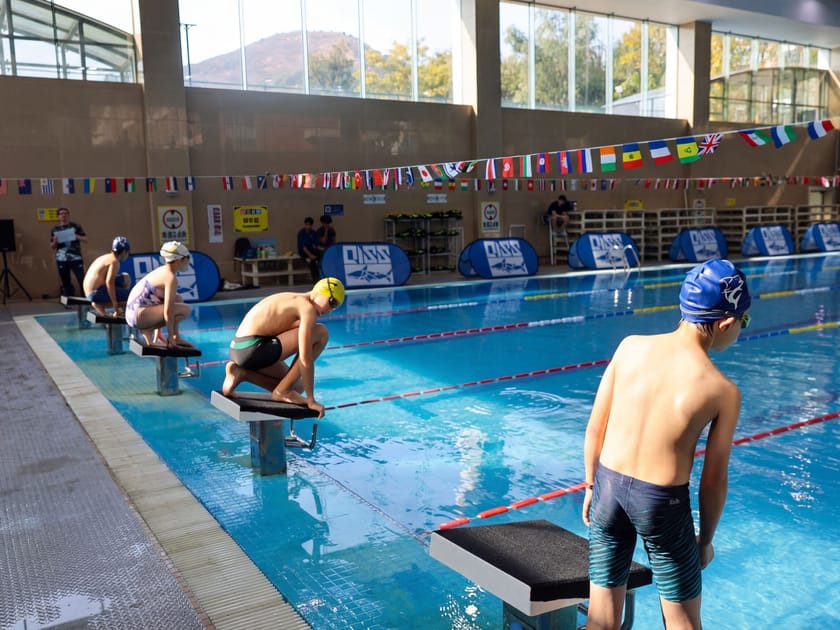 Diversity and Inclusion in International Schools 2 Young swimmers from QISS stand on diving boards at an indoor pool with international flags displayed on the wall, symbolizing a globally inclusive school community