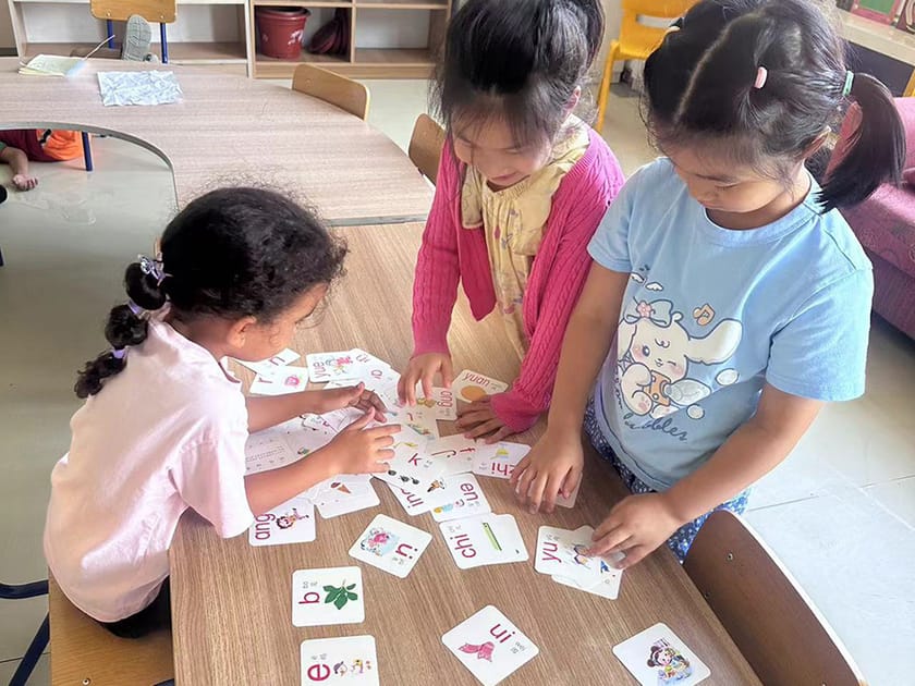 ELL Programs: Supporting Non-Native English Speakers 3 Young QISS students using literacy flashcards together, illustrating the kind of structured language support parents should look for in an ELL program