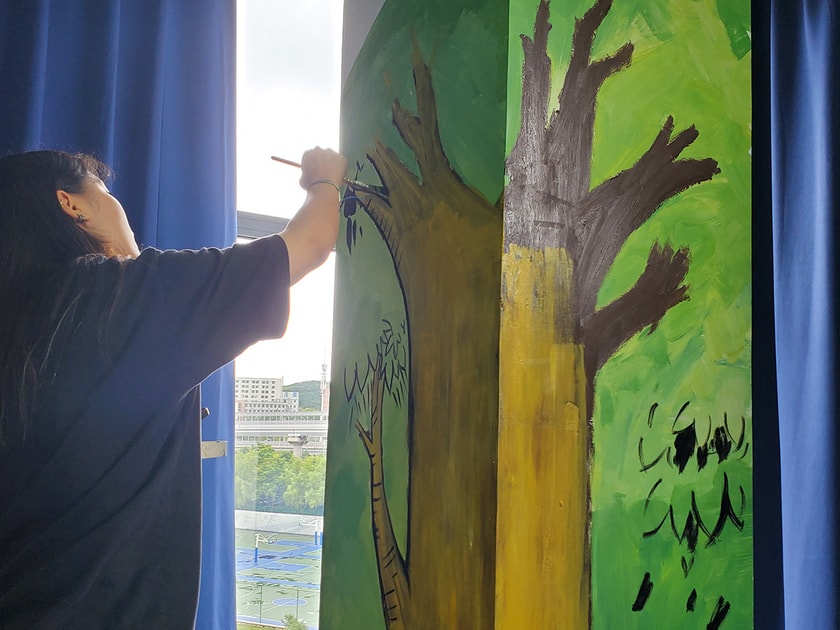 Academic Pressure on Students: Causes, Effects & Support 2 A student standing on a stool painting a large green tree mural, illustrating creative expression as a practical coping strategy for academic stress