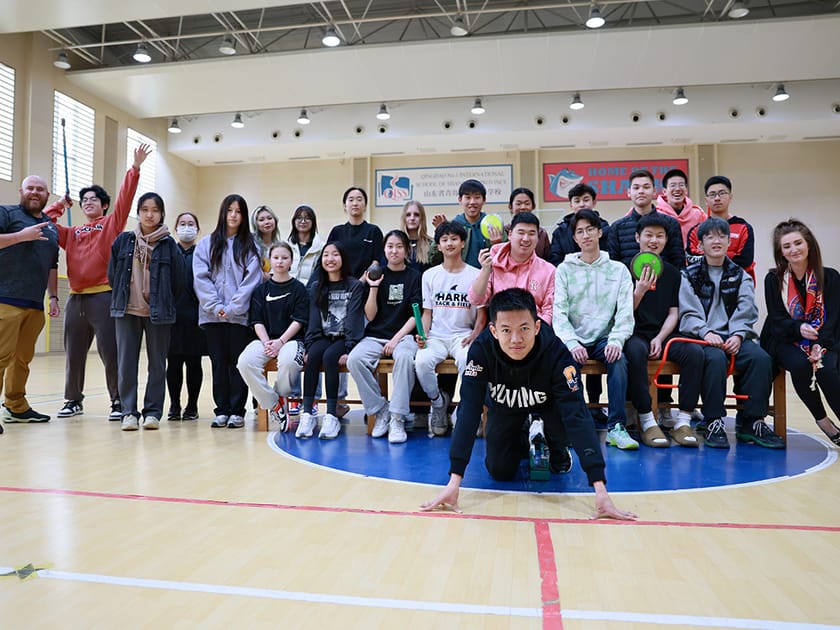 Middle School Transition: Supporting Students Through Change 2 A QISS teacher poses with a large group of middle school students in the gymnasium, illustrating the school's hands-on, community-oriented support approach