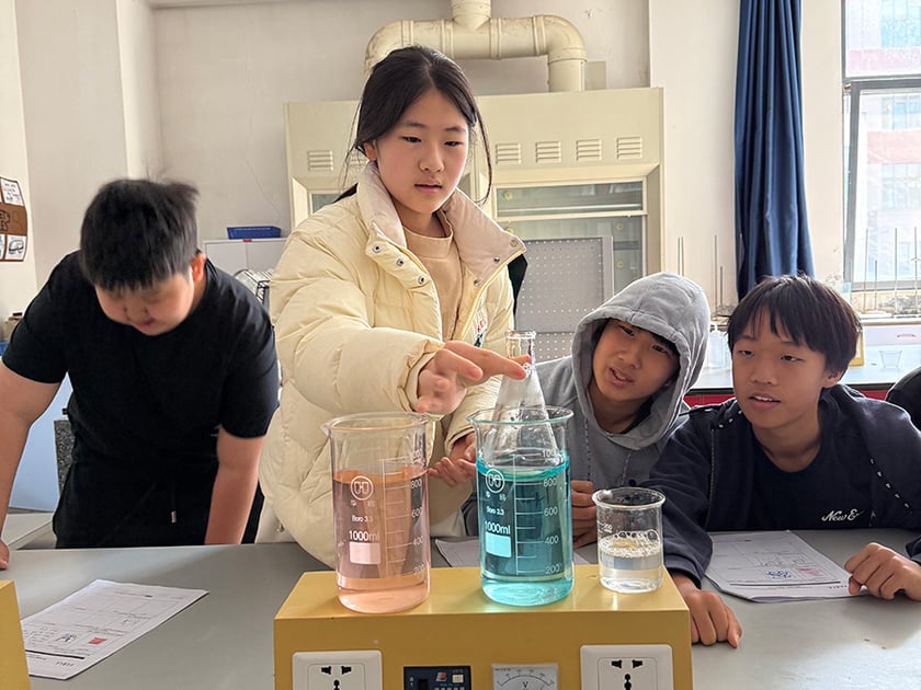 Middle school students conduct a chemistry experiment with colored solutions in a QISS science lab, guided by their teacher.