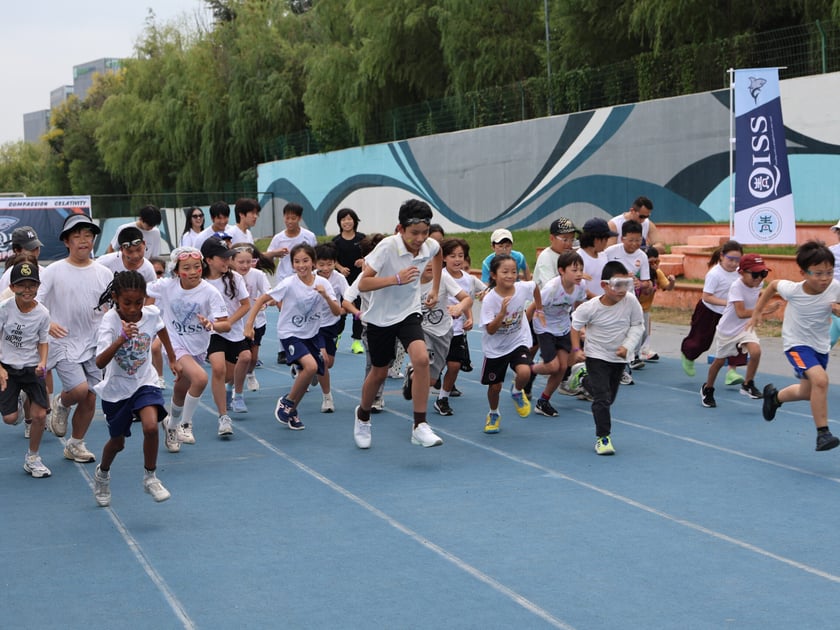 Student Wellbeing in Schools: What Actually Works 2 Lower school students in white t-shirts run together on a blue athletic track supervised by teachers during an outdoor school event