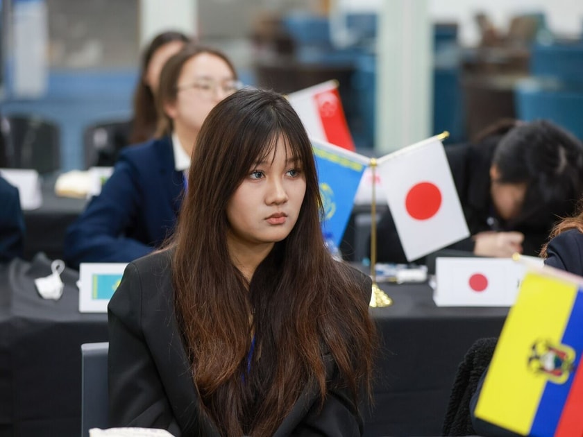 High school student at a Model UN conference table with international country flags, representing global ambitions of Chinese students