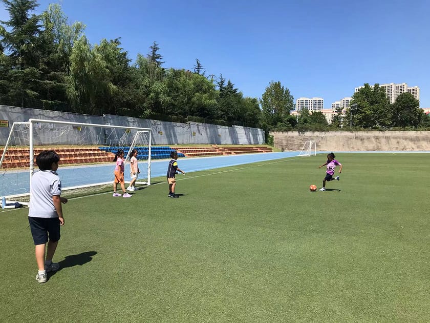 After School Activities: What the Research Says 3 Elementary-age students practicing soccer on an outdoor turf field at QISS, showing younger children engaged in a structured after-school sports activity