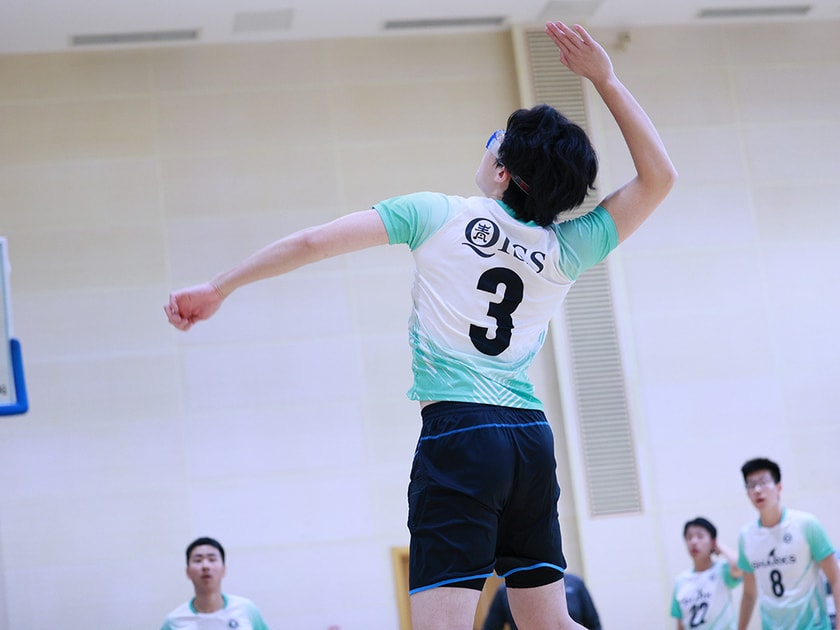 Student athlete in turquoise volleyball uniform jumps to spike the ball during a competitive school gym match