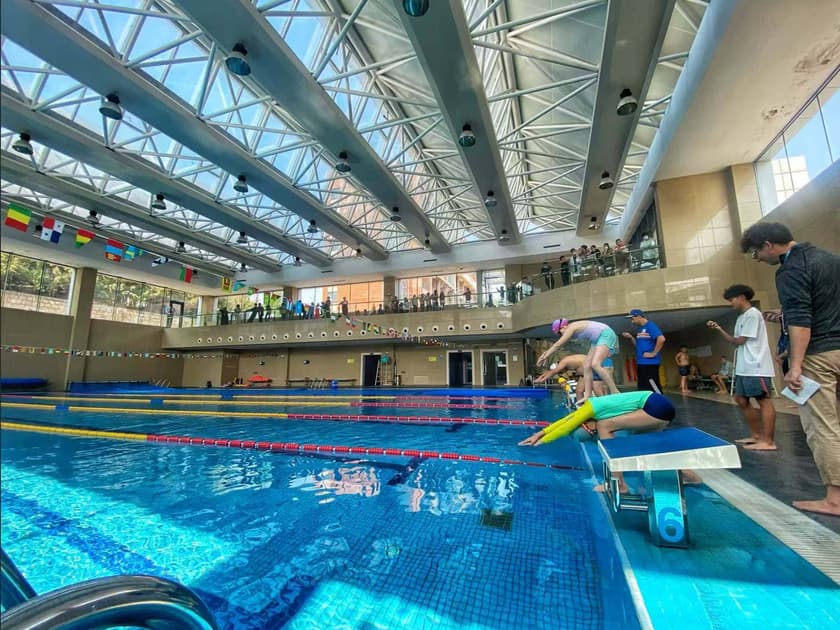 School Athletics Programs: Sports for Every Student 2 QISS students competing in a swimming and diving event in the school's modern indoor aquatic facility