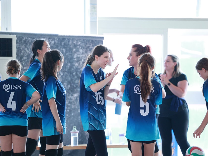 Summer Camp at an International School: What to Expect 2 Girls volleyball team huddles with their coach during an indoor gym session at an international school athletics program