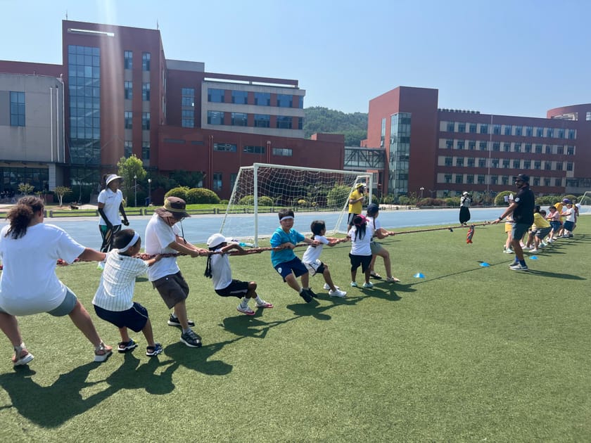 Outdoor Learning Spaces: How Schools Bring Nature In 2 Lower school students doing tug-of-war on a sunny outdoor field at an international school
