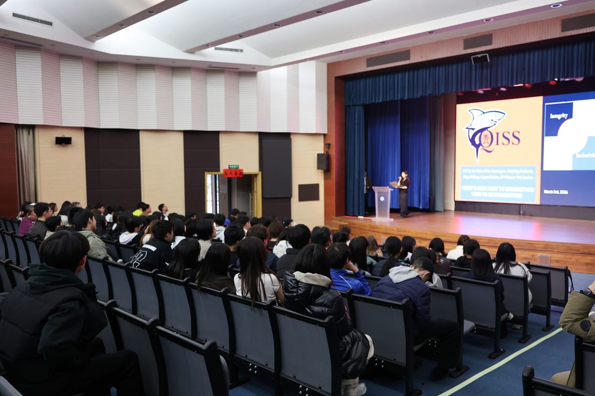 AP Courses China: Guide for Qingdao International Students 1 QISS high school students seated in the school auditorium during a student-led assembly, with the QISS logo and school values shown on the presentation screens.