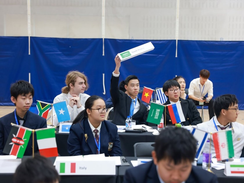 School Counselors: Roles, Support, and Student Outcomes 3 High school student raises hand to speak at Model UN conference with country flags