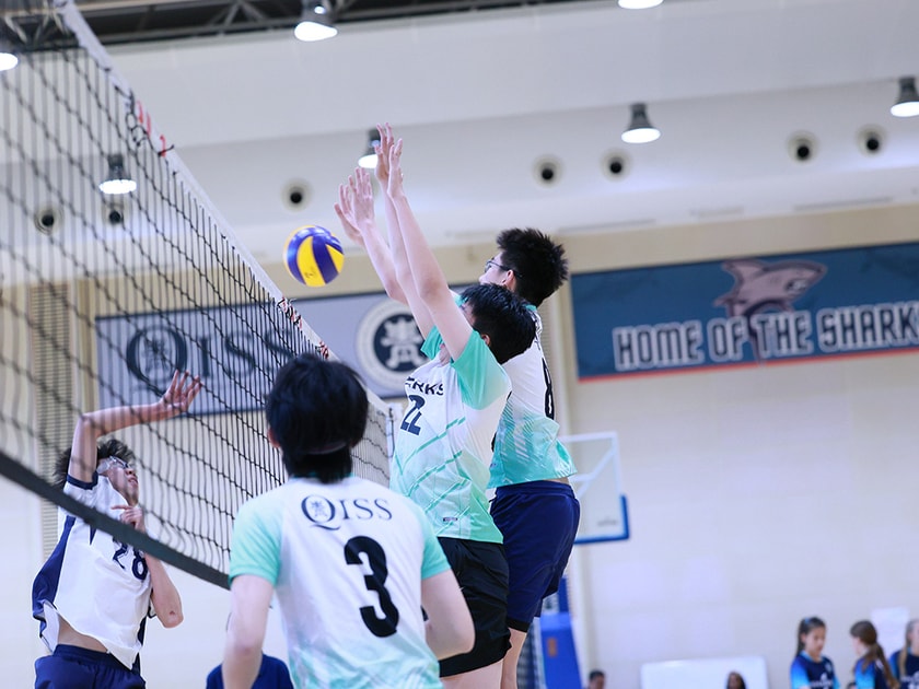 Middle school volleyball players jump at the net in the Home of the Sharks gymnasium