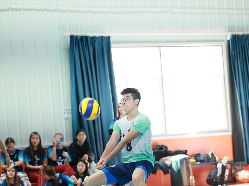 School Sports Facilities and Student Development 3 QISS student in volleyball uniform passing ball during daily gym class with teammates watching