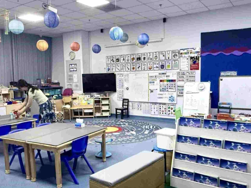 When Your Child Struggles with Maths: A Parent's Guide 1 Teacher arranges materials in a bright early-childhood STEM classroom with planet mobiles and educational displays