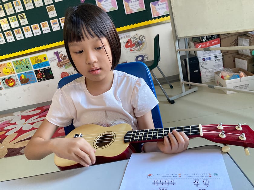 Young student concentrates independently on guitar sheet music in a colourful lower-school classroom