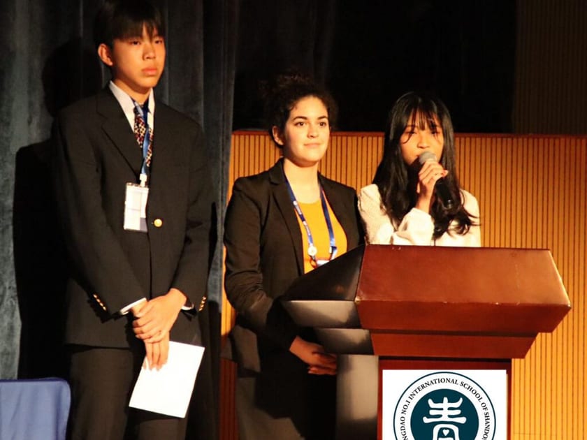 Applying to Australian Universities from China: What Students Should Know 2 Three QISS high school students in blazers stand at a podium with the QISS logo during a presentation