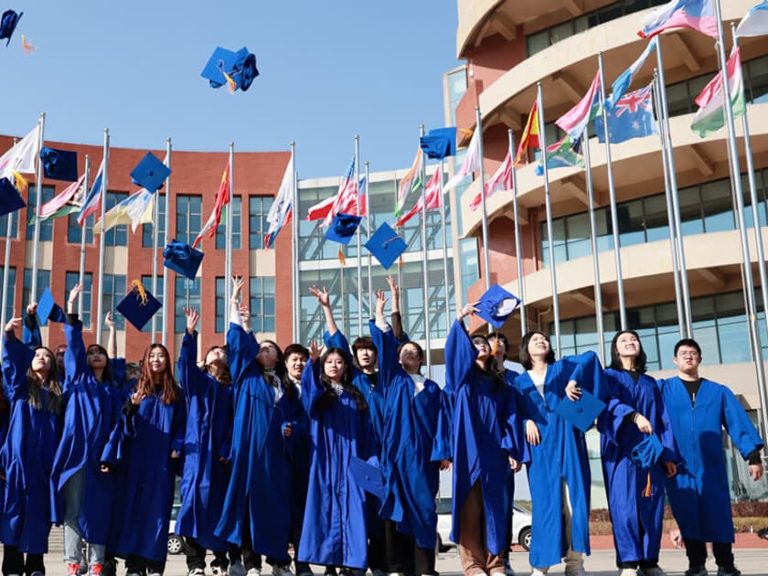 Applying to Universities in Japan from China: A Guide for International School Students 1 QISS graduates in blue gowns throw their caps into the air in front of the campus flagpoles