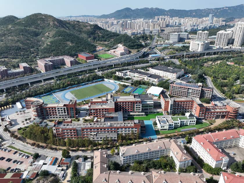 Gaokao vs SAT: What International School Families Should Know 1 Aerial view of the QISS campus in Laoshan, Qingdao, with its sports field and the city beyond