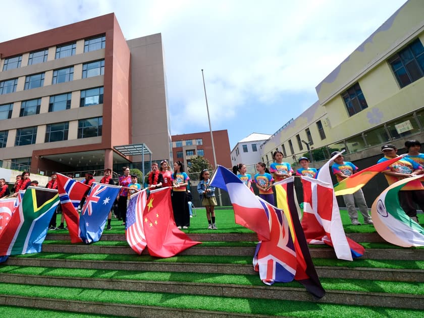 International Day at School: What Parents Should Know 2 Students and adults hold flags from many countries on the courtyard steps at QISS International Day