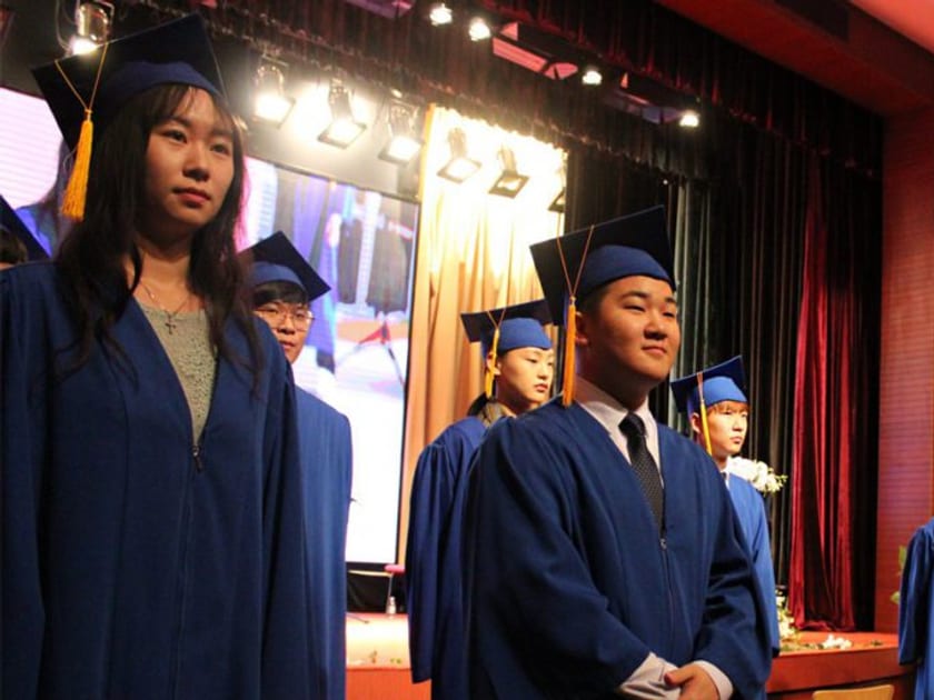 한국 대학 입시 가이드: 국제학교 학생을 위한 재외국민·외국인 특별전형 2 학사모와 가운을 갖춘 QISS 졸업생들이 졸업식 강당 무대 위에 나란히 서 있습니다