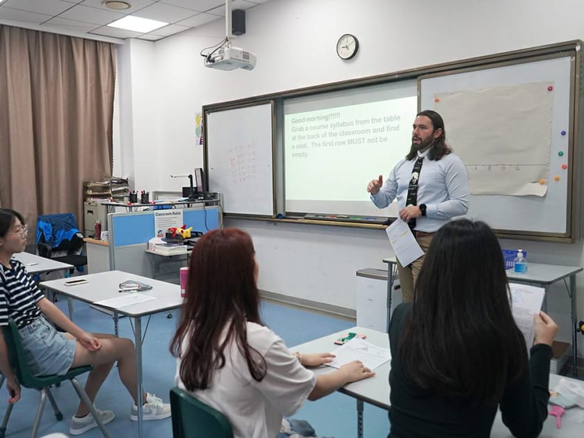The Chinese School System Explained: Grades, Ages and US Grade Equivalents 2 A teacher in a shirt and tie talks to secondary students seated at classroom desks in front of a projected welcome message